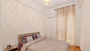 Een slaapkamer met een bed, nachtkastje, een luchtverkoeler aan de muur en een raam met gordijnen.