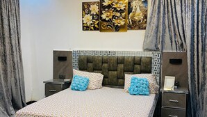 Un dormitorio con cama, mesitas de noche, cabecero, una obra de arte en la pared y cortinas.