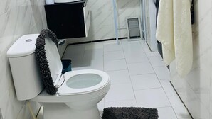 Un baño con inodoro, lavamanos y estante con artículos de aseo.