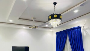 Un salón moderno con un televisor de pantalla plana, un ventilador de techo, una araña y cortinas azules.