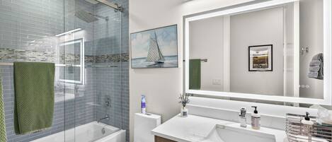 A modern bathroom with a glass shower enclosure, a toilet, a sink with a large mirror, and a framed picture on the wall.