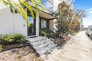 Un bâtiment moderne avec un escalier en béton menant à une porte, entouré de verdure et sous un ciel dégagé.