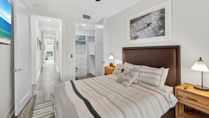 Ein Schlafzimmer mit einem Bett, Nachttischen, einem Deckenventilator, einem an der Wand hängenden Bild und einem Flur, der zu einem Kleiderschrank führt.