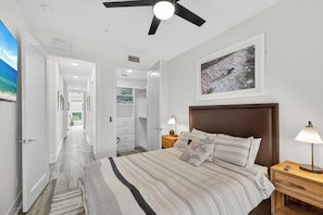 A bedroom with a bed, nightstands, a ceiling fan, a wall-mounted picture, and a hallway leading to a closet. - 52 audubon (Sarasota)