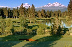 A golf course with a lake, trees, and snow-capped mountains in the background. - Walk to Town, Mountain Views, Hot Tub, Dogs OK (Sisters)