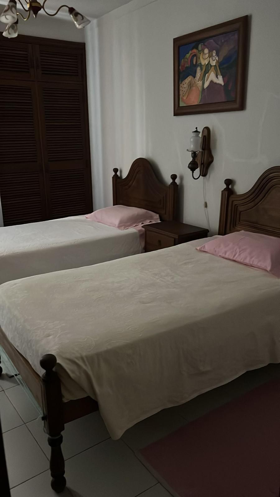 A bedroom with two beds, a nightstand, a telephone, and a painting on the wall.