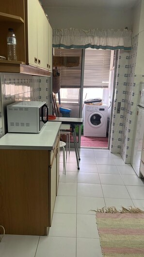 A compact kitchen with a washing machine, a refrigerator, and a dining area with a table and chairs. - Portimão Beach Apartment (Portimão)