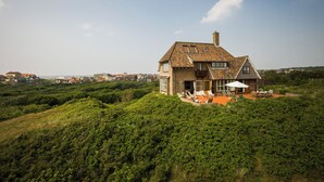 A house with a sloped roof, a chimney, and a patio with outdoor furniture. - Villa de Duintop (12 people) A dream vacation home on a dune. (Bergen aan Zee)