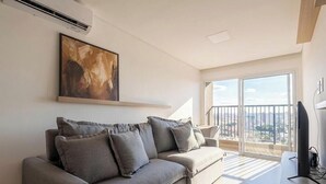 A modern living room with a grey sofa, a mounted artwork, a flat-screen TV, and a balcony with a city view. - Apt. in Condo. w/ Pool in Anapolis Grlb1405 (Anapolis)