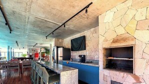 A modern kitchen with a stone backsplash, a built-in oven, and a bar area with stools. - Apart in a Cond. With Pool in Guarajuba Atv0110 (Camaçari)