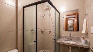 A modern bathroom with a glass-enclosed shower, a sink with a marble countertop, and a mirror with a wooden frame. - Apart in a Cond. With Pool in Guarajuba Atv0110 (Camaçari)