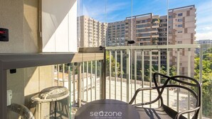 A balcony with a chair, a fan, and a view of high-rise buildings. - Modern Studio in Moema Ois10623 (São Paulo)