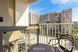 Ein Balkon mit einem Stuhl, einem Ventilator und Blick auf hohe Gebäude.