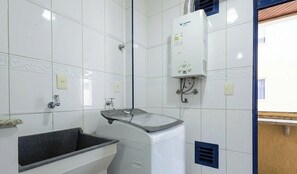 A bathroom with white tiled walls, a sink with a mirror, a shower, and a white water heater. - Apt in Building w/ Sea View in Itapema Clzb0504 (Itapema)