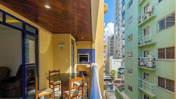 A narrow outdoor space with a glass table and chairs, a small blue-tiled fireplace, and a wooden ceiling. - Apt in Building w/ Sea View in Itapema Clzb0504 (Itapema)