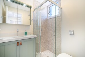A bathroom with a glass shower enclosure, a white sink, and a mirror above it. - Modern Studio in Downtown Florianopolis Eva0504 (Florianópolis)