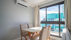 Ein Hotelzimmer mit Esstisch, Stühlen, einer Sitzecke und einem großen Fenster mit Blick auf Gebäude, sowie einer Klimaanlage.