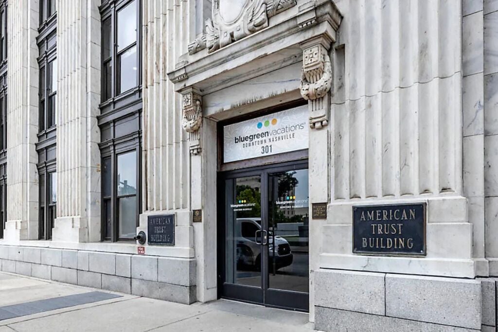 Un immeuble avec une enseigne indiquant « Bluegreen Vacations », une plaque commémorative pour l’« American Trust Building » et une caméra de surveillance.