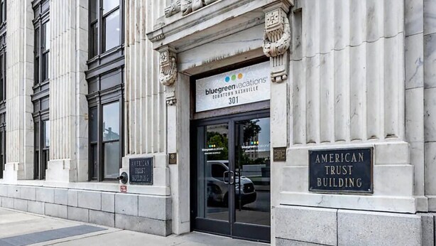 Un immeuble avec une enseigne indiquant « Bluegreen Vacations », une plaque commémorative pour l’« American Trust Building » et une caméra de surveillance.