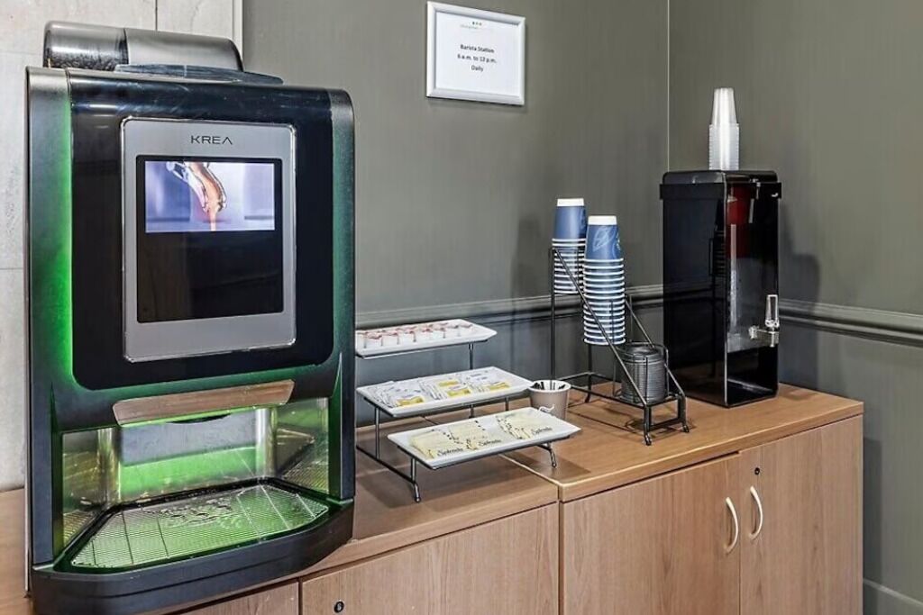 Une machine à café KREA dotée d’un écran numérique, d’un distributeur de café et d’un panneau de commande sur un comptoir en bois.