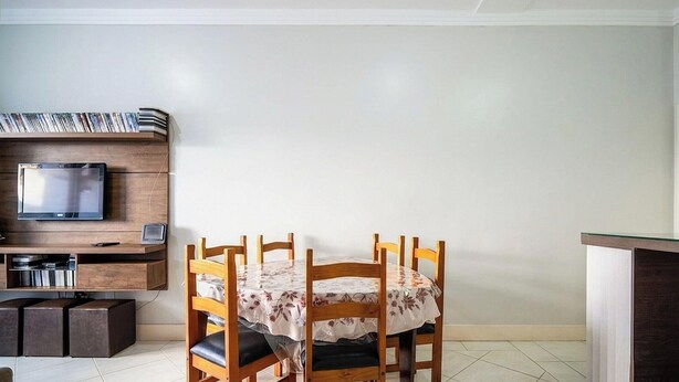 Un comedor con una mesa preparada para cuatro, un televisor montado en un panel de madera y un mueble bajo el televisor.