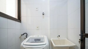 Baño pequeño con pared de azulejos blancos, lavadora integrada, lavamanos y una puerta con cerradura.