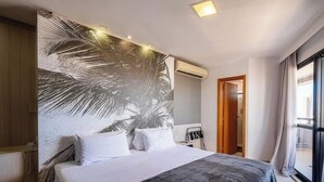 Una camera d'albergo con un letto grande, un affresco, una finestra con tende e una porta che conduce a un'altra stanza.