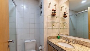 A bathroom with a toilet, a sink, a mirror, and shelves with toiletries. - Studio in Condo. w/ Pool in Downtown Nwc1007 (Curitiba)