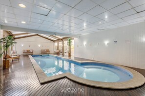 An indoor swimming pool with wooden flooring, lounge chairs, and a tiled wall. - Studio in Condo. w/ Pool in Downtown Nwc1007 (Curitiba)