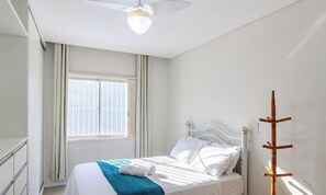 Ein Hotelzimmer mit einem Bett, einem Fenster mit Vorhängen, einem Deckenventilator und einem Kleiderständer.