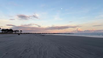 Une vaste plage de sable, parsemée d’empreintes, un ciel dégagé et une lune en croissant.