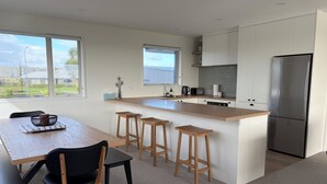 Een moderne keuken met een centraal eiland, barstoelen, een eettafel met stoelen en een koelkast.