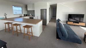 Een moderne keuken met een centraal eiland, barkrukken, een koelkast en een televisie in een woonruimte met een bank.