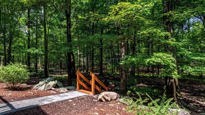 A forested area with a wooden bridge, a stone pathway, and a small wooden structure.