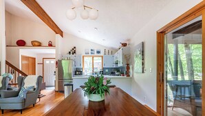 A spacious living room with a wooden dining table, a grey armchair, and a staircase leading to another level.