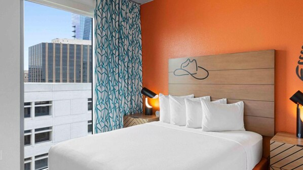 A hotel room with a large bed, a nightstand with a lamp, a patterned curtain, and a city view.