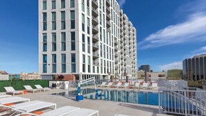 A high-rise hotel with a rooftop pool, lounge chairs, and a clear blue sky.