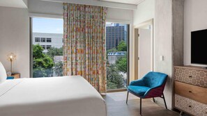 A hotel room with a bed, a blue chair, a television, and a view of buildings and greenery through the window. - Downtown Austin Stay Near Dining, Music & Spacious 2BR Resort Suite (Austin)