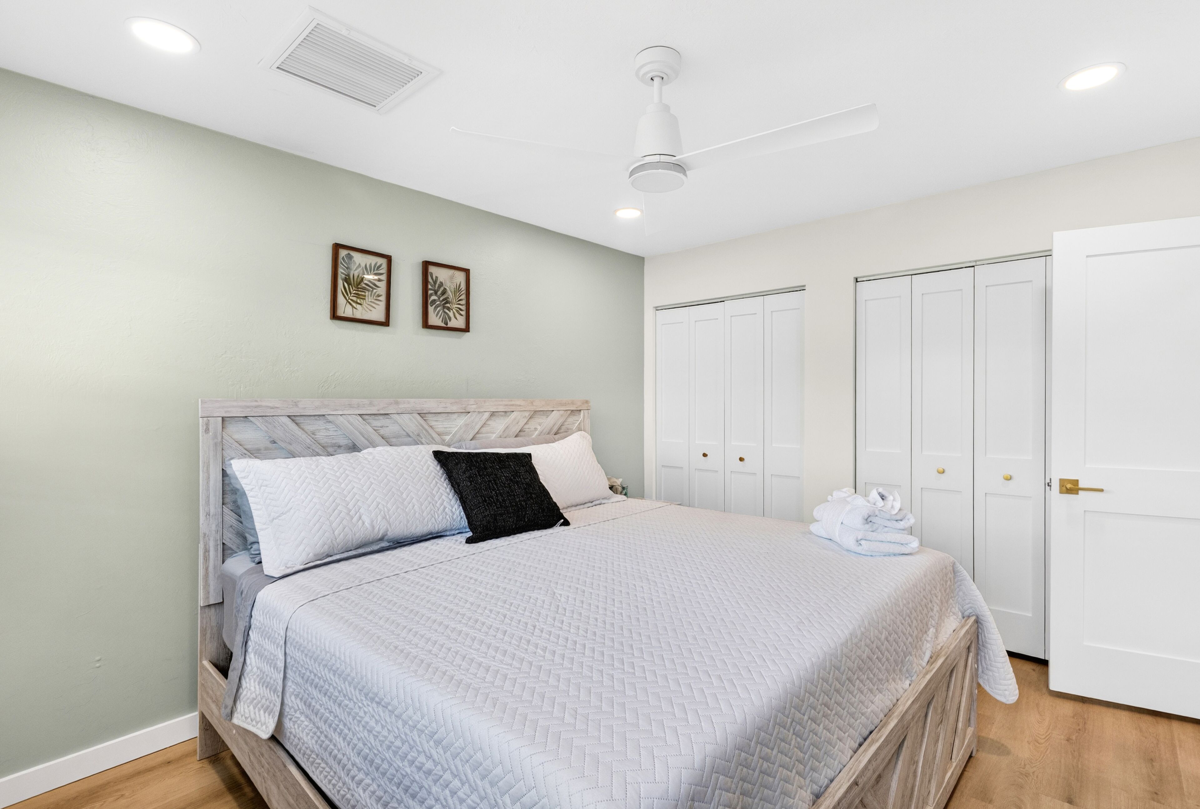 A bedroom with a bed, a ceiling fan, a wardrobe, and two framed pictures on the wall.