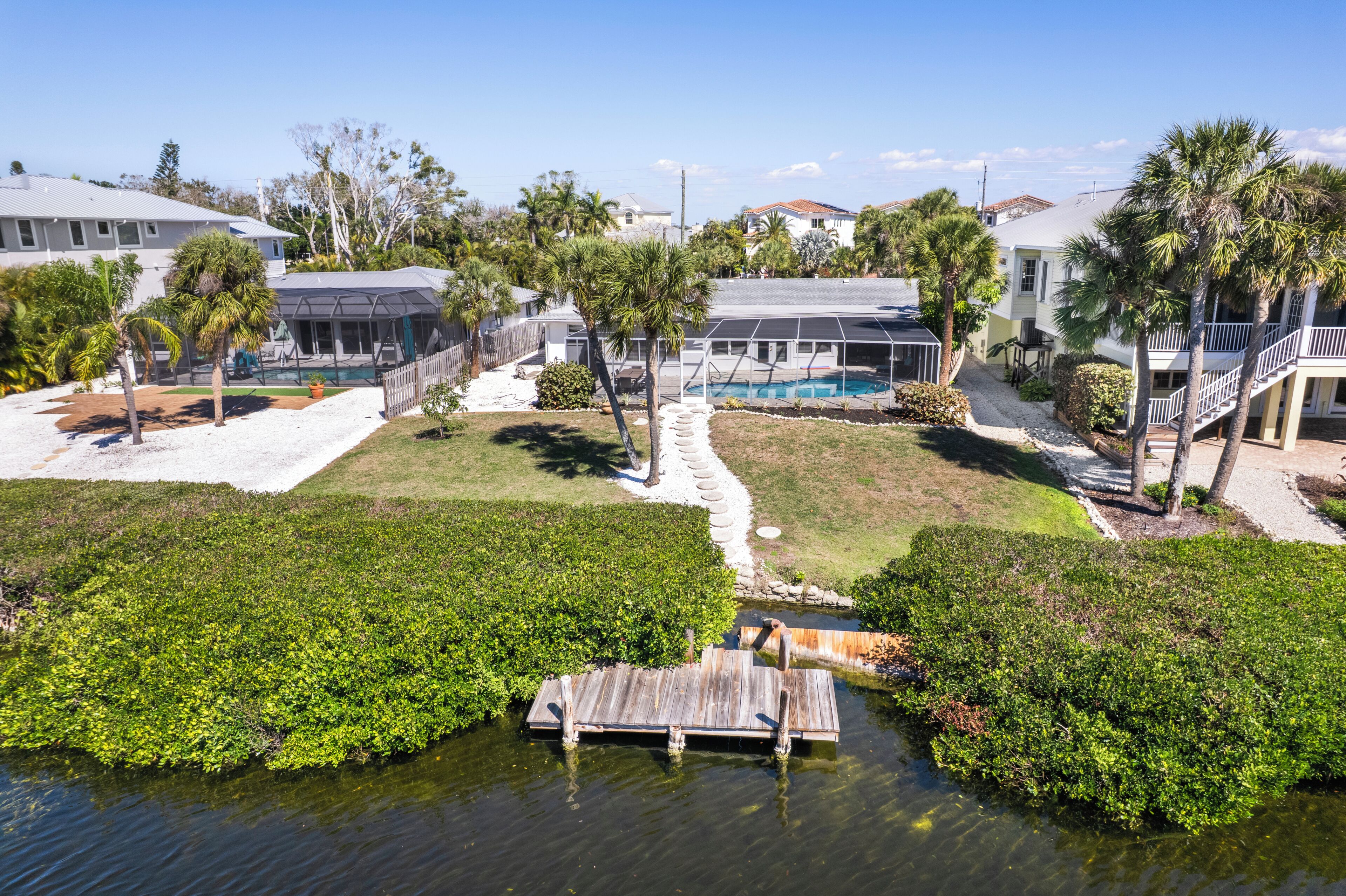 A residential area with a swimming pool, palm trees, and a dock over water.