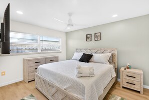 A bedroom with a bed, a nightstand, a dresser, a ceiling fan, and a window with blinds. - Waterfront Home with Pool First Floor (Sarasota)