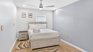 A bedroom with a bed, nightstands, a ceiling fan, and a window with blinds. - Waterfront Home with Pool First Floor (Sarasota)