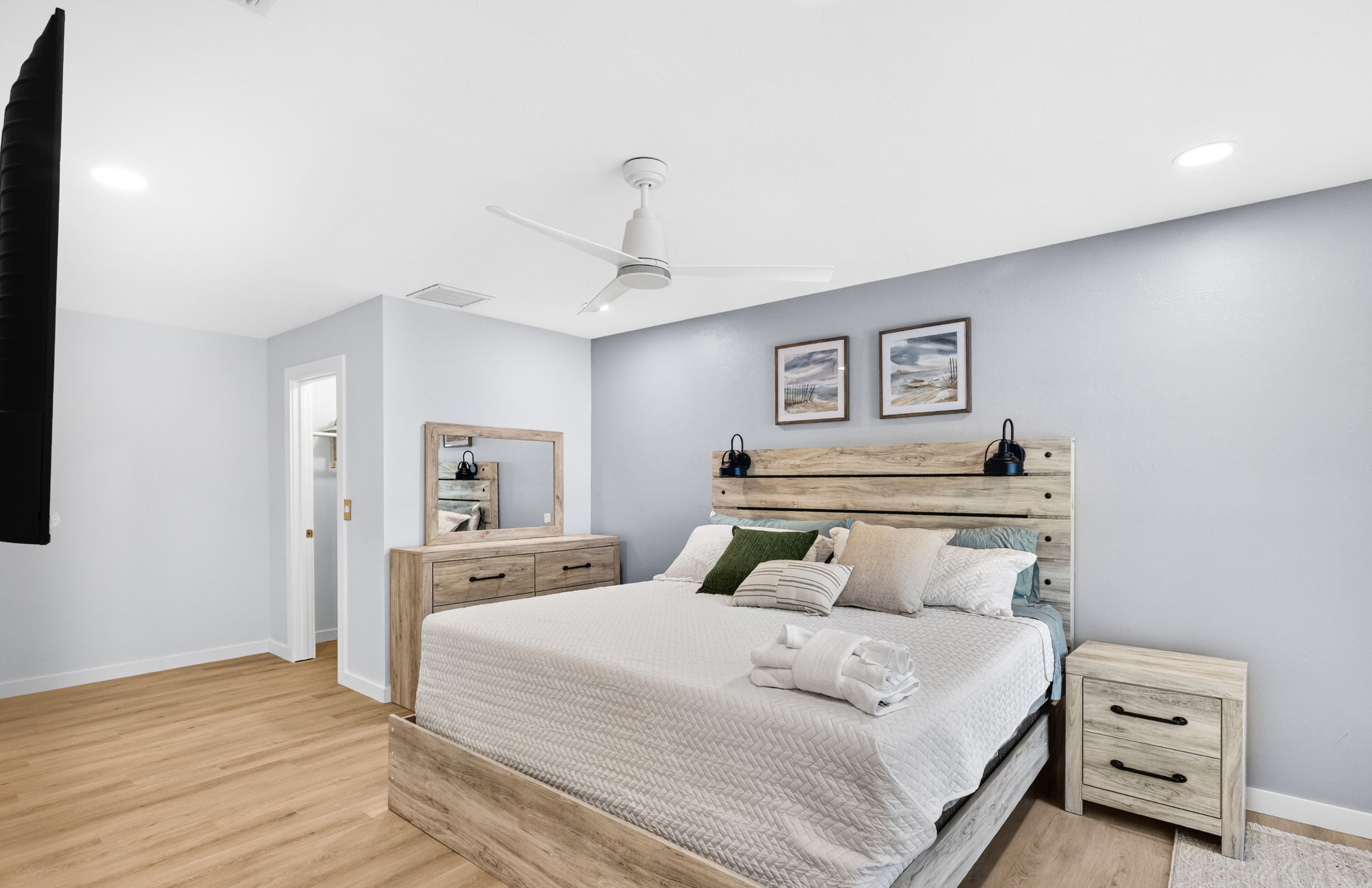 A bedroom with a bed, bedside tables, a ceiling fan, and artwork on the wall.