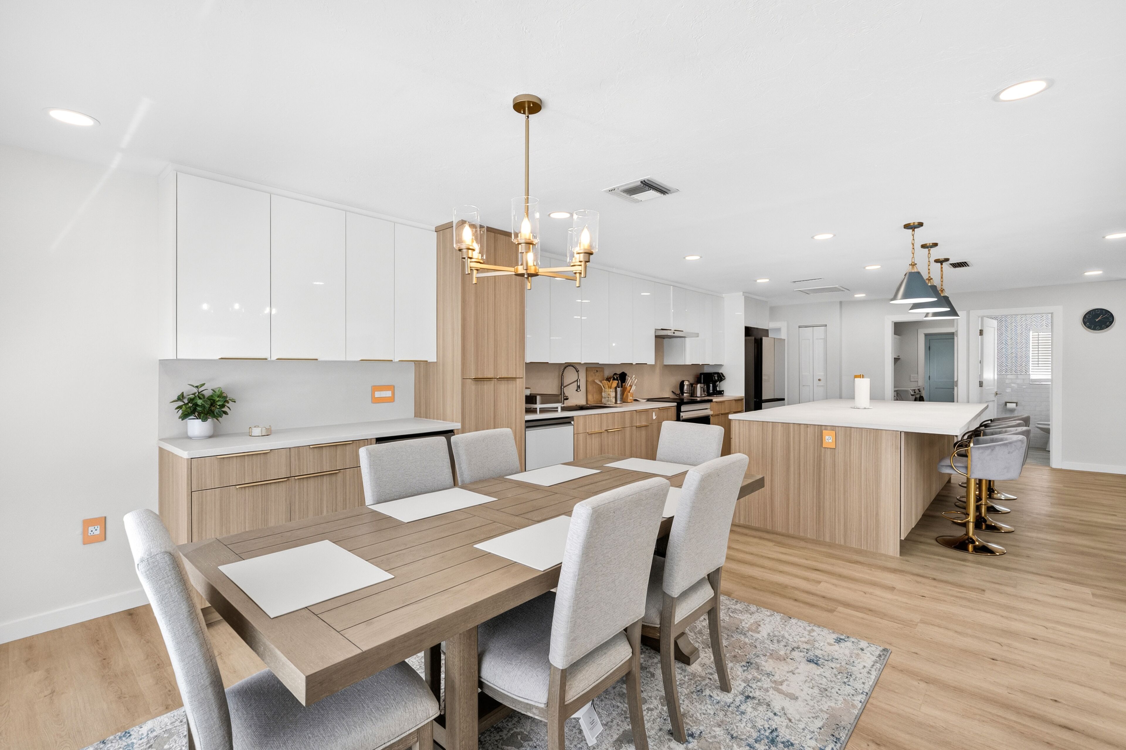 Una cocina moderna con armarios blancos, una mesa de comedor de madera y una araña.