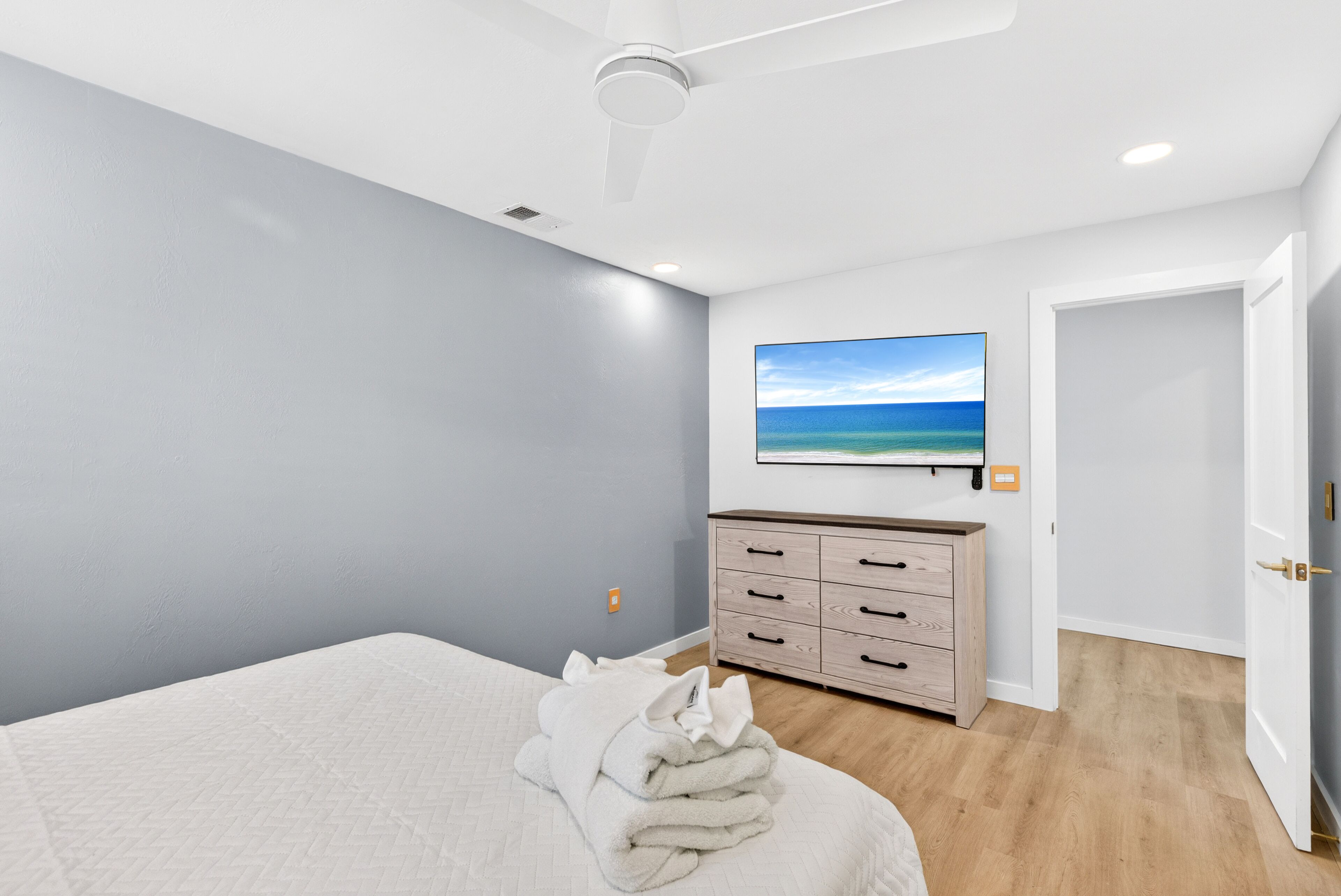 A bedroom with a bed, a dresser, a television mounted on the wall, and a door.