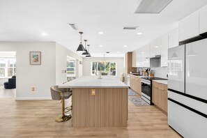 A modern kitchen with a central island, wooden cabinets, and a large window. - Waterfront Home with Pool First Floor (Sarasota)