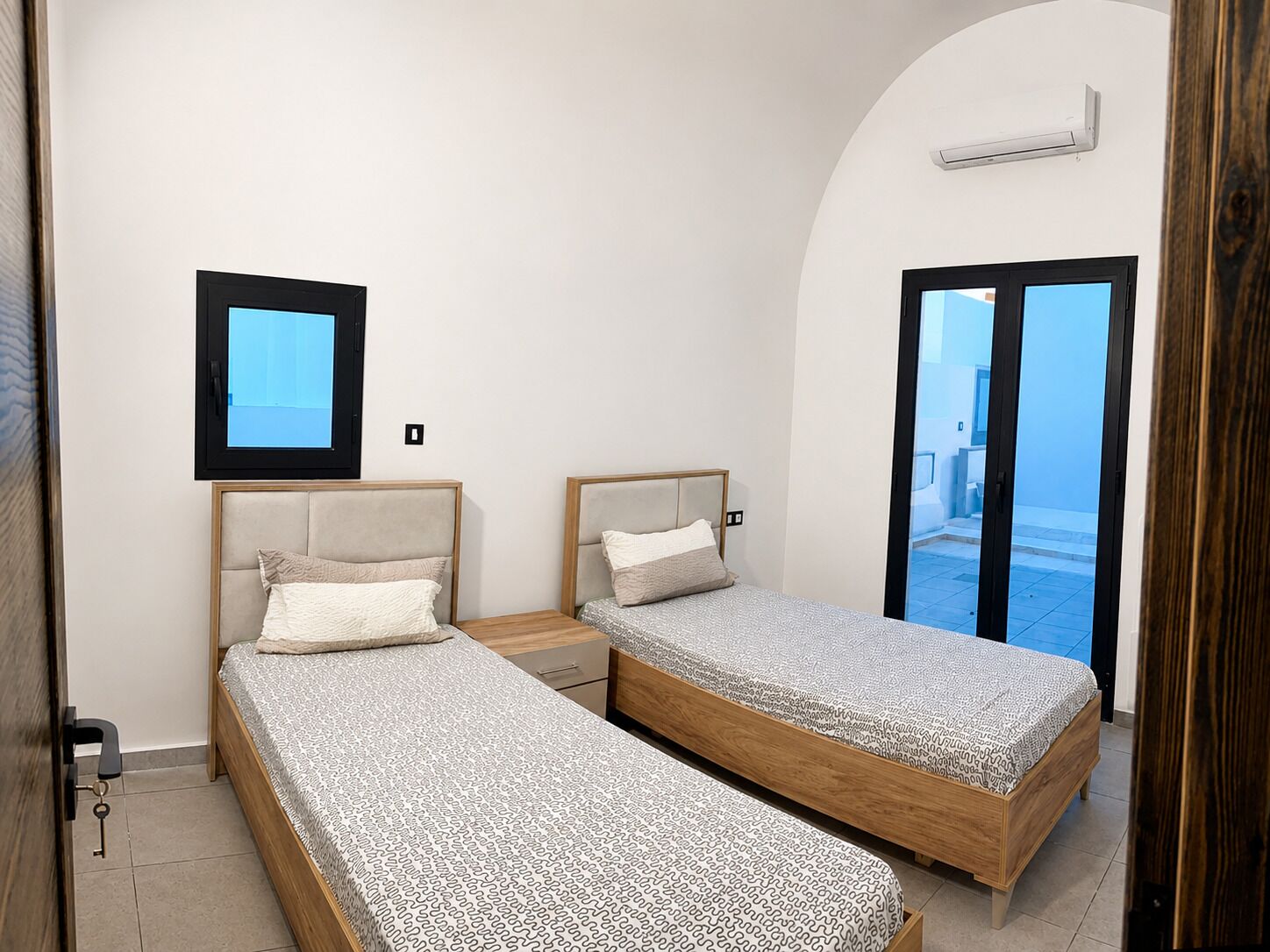 Une chambre avec deux lits, une petite fenêtre et une vue sur l’extérieur.