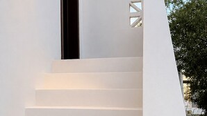 Een witte trap met een geometrisch uitgesneden ontwerp in de muur, leidend naar een donkere deuropening.