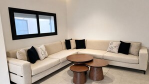 Een moderne woonkamer met een beige modulaire bank, twee houten salontafels en zwart-wit gestreepte sierkussens.