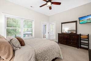 Quarto com cama, cômoda, ventilador de teto e uma grande janela com persianas.